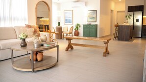 Een moderne woonkamer met een ronde salontafel, een bank, een houten zitbank en een eethoek met stoelen en een tafel.
