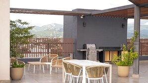 Un patio al aire libre con una mesa, sillas, una parrilla y plantas en macetas.