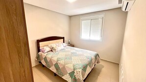 A bedroom with a bed, a window with blinds, and an air conditioning unit on the wall. - Beautiful apartment located on Bombas Beach 🐶️ Sleeps up to 8 people (Bombinhas)