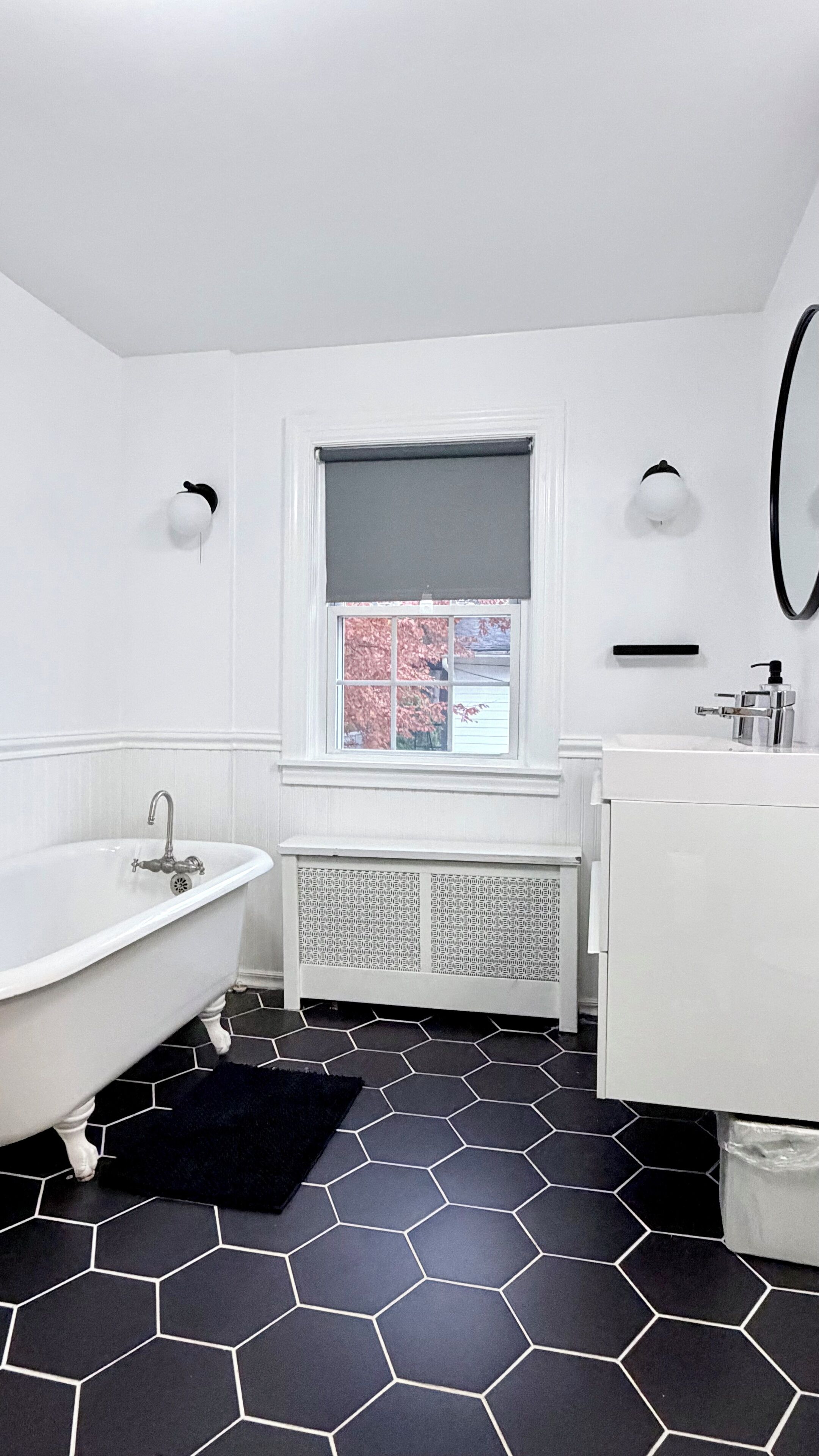 Un baño con una bañera blanca, un lavabo blanco y una ventana con vistas a árboles rosados.