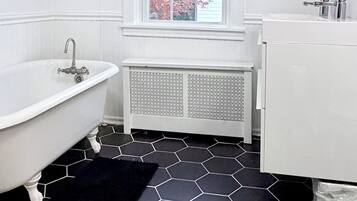 Un baño con una bañera blanca, un lavabo blanco y una ventana con vistas a árboles rosados.