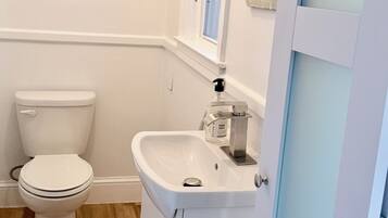 Une salle de bain avec des toilettes blanches, un lavabo blanc doté d’un distributeur de savon et un tableau encadré au mur.