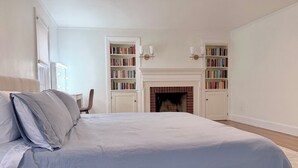 Un dormitorio con una cama grande, dos estanterías, una chimenea y una silla.