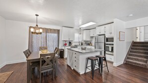 Une cuisine moderne avec des meubles blancs, un îlot central et un coin repas comprenant une table et des chaises en bois.