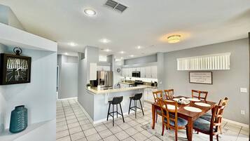 Une cuisine moderne avec des meubles blancs, un réfrigérateur en acier inoxydable et un îlot central doté de tabourets de bar.
