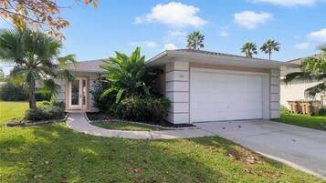 A single-story house with a garage, surrounded by a well-maintained lawn and palm trees.