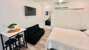 Une chambre à coucher comprenant un lit, un bureau avec une chaise, un canapé noir, un ventilateur de plafond et une armoire.