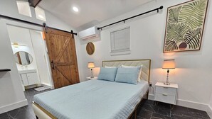 Une chambre à coucher comprenant un lit, une table de chevet, un miroir, une armoire et un climatiseur fixé au mur.