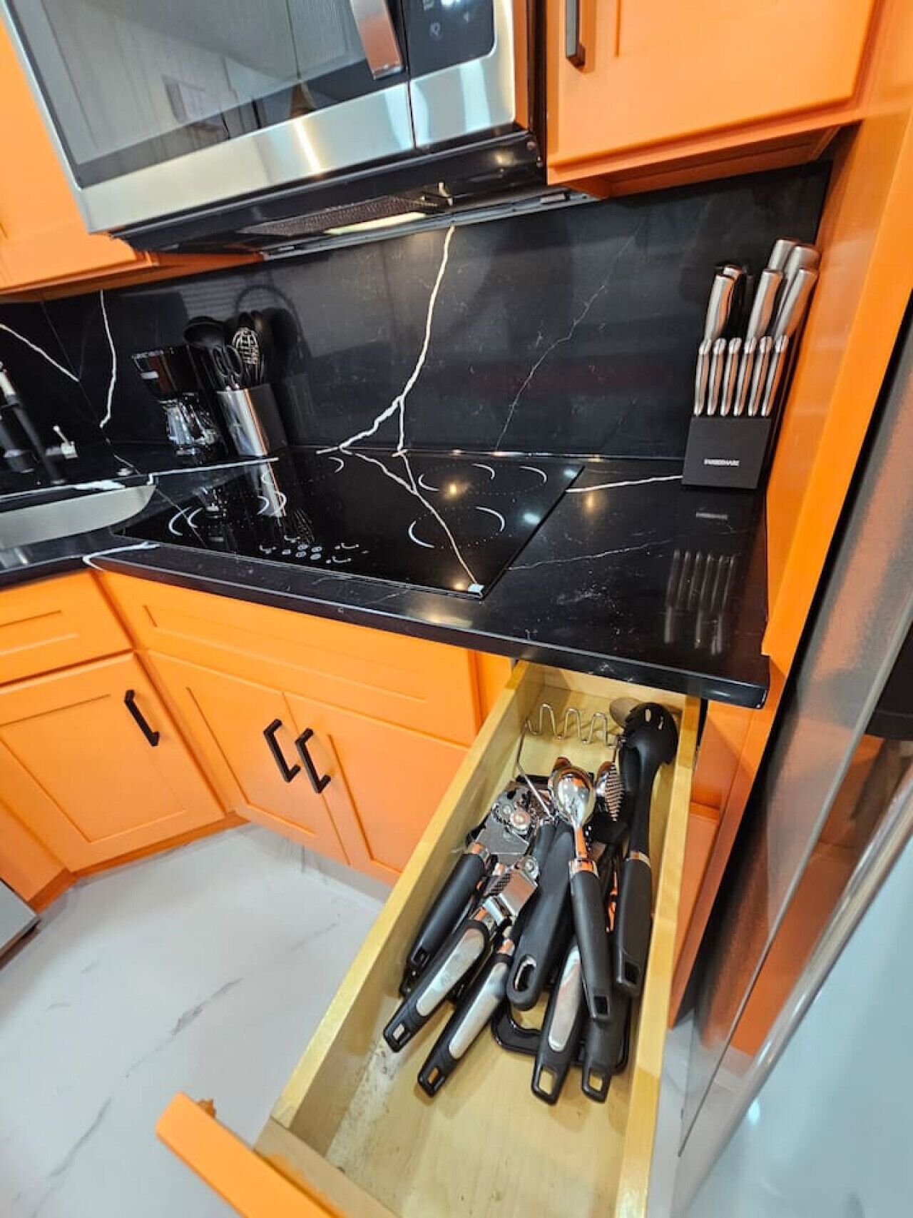Uma cozinha com bancada preta, eletrodomésticos de aço inoxidável e armários laranja.