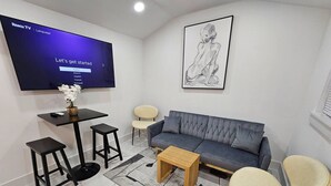 Un salon moderne avec un canapé gris, des chaises noires et blanches, une petite table basse en bois et un téléviseur à écran plat fixé au mur.