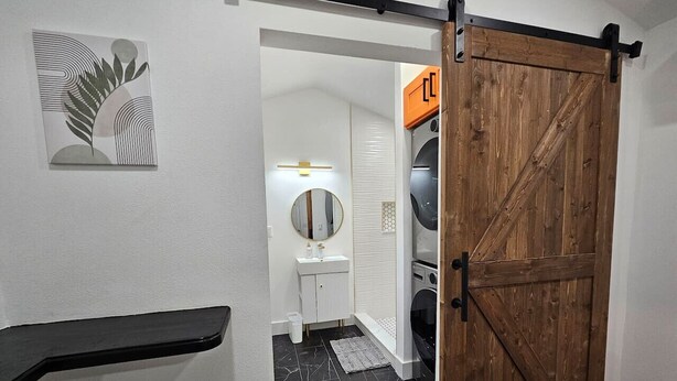 Une salle de bain moderne avec une porte en bois, un lavabo blanc et un miroir.