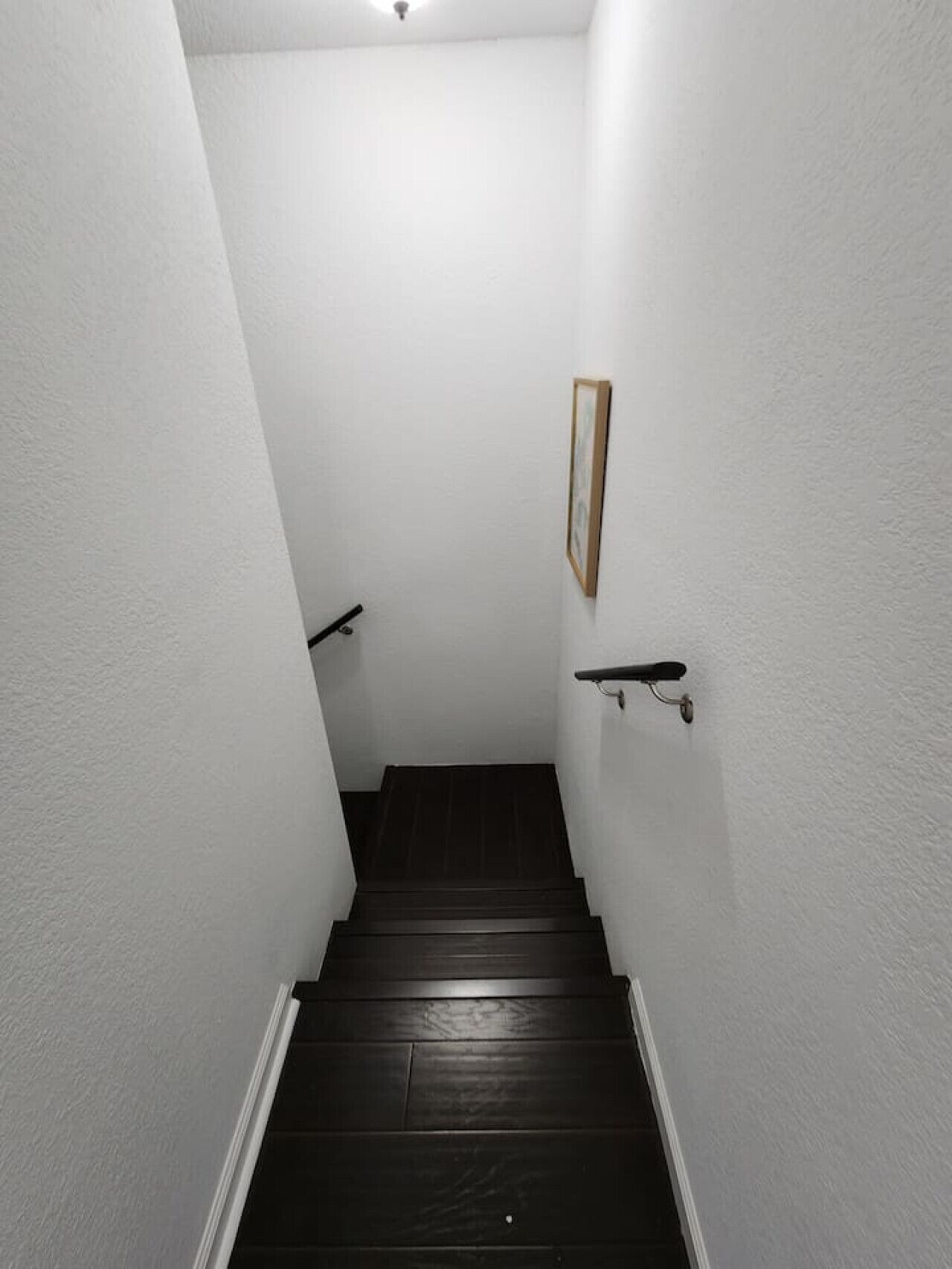Un escalier étroit aux murs blancs et aux marches en bois foncé.
