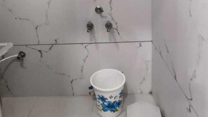 Um banheiro pequeno com azulejos de mármore branco, chuveiro, vaso sanitário e um banquinho.