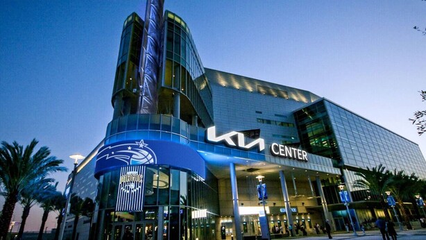 Un bâtiment moderne avec une façade en verre, une grande enseigne « KIA Center » bien visible et une enseigne « Magic » sur le niveau inférieur.