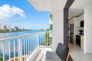A balcony with a view of a river and city skyline, a modern kitchen, and a seating area with a sofa and table. - Condado: 1 Block to Beach, Scenic Bay Balcony (San Juan)