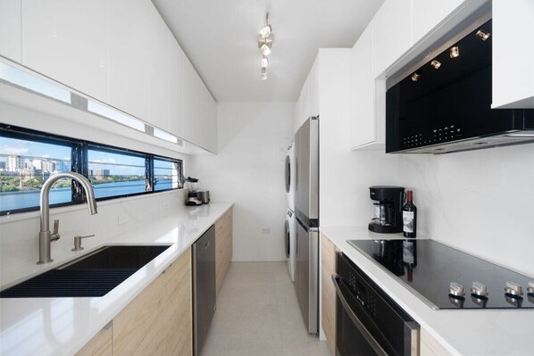 A modern kitchen with a view of a river, a built-in dishwasher, a coffee maker, and a wine bottle. - Condado: 1 Block to Beach, Scenic Bay Balcony (San Juan)