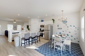 Una cocina moderna con armarios blancos, electrodomésticos de acero inoxidable y un comedor con sillas blancas y un tapete azul.
