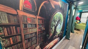 Een bibliotheek met boekenkasten en een muurschildering van een boom.