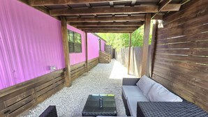 Een terras buiten met een overdekte zithoek, een tafel en een houten omheining.