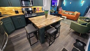 Een moderne keuken met donkergroene kastjes, een houten eettafel en barstoelen.