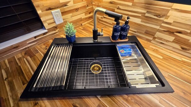 Een keuken met een zwart spoelgootsteentje, een houten aanrechtblad en een kleine potplant.