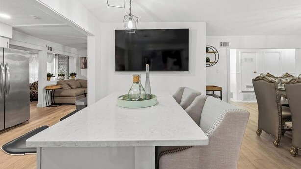 Una cocina moderna con una isla central, un comedor con candelabro y una sala de estar con sofá y televisor.