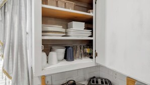 Una cocina con armarios blancos, encimera de madera y cortina blanca con detalles amarillos.