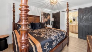 Una cama con dosel adornada con una colcha negra y dorada, un cabecero de madera y una lámpara en el techo.