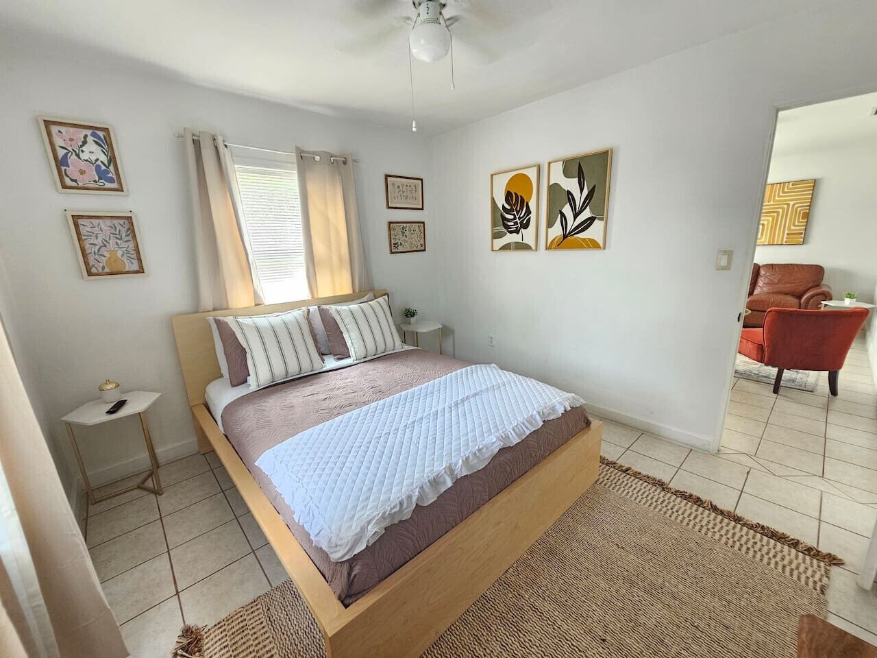 Een slaapkamer met een bed, nachtkastje, gordijnen en een kunstwerk aan de muur.