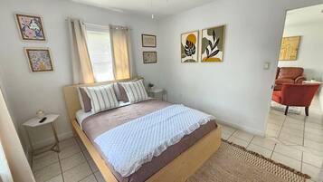 Een slaapkamer met een bed, nachtkastje, gordijnen en een kunstwerk aan de muur.