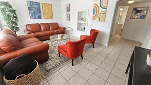 Un salon avec un ensemble de canapés en cuir marron, un fauteuil rouge et une table basse. Les murs sont ornés de tableaux abstraits et un pot de fleurs se trouve dans un coin.