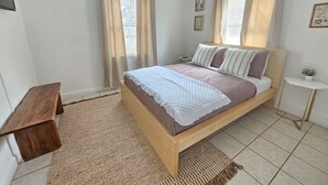 Une chambre à coucher avec un lit, une table de chevet, une petite table ronde et une fenêtre avec des rideaux.