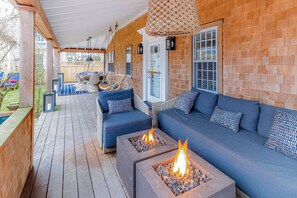 A covered outdoor seating area with a wooden deck, blue sofas, and two square fire pits with flames. - Close to Dtwn Nantucket! Group Getaway w/ Patio (Nantucket)