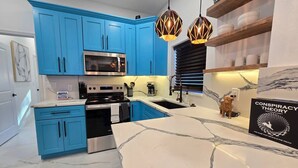 Eine moderne Küche mit blauen Schränken, einer weißen Marmorarbeitsplatte, Edelstahlgeräten und Pendelleuchten.