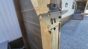 Ein Metallriegel an einer Holztür, ein Betonboden und ein Kiesweg.