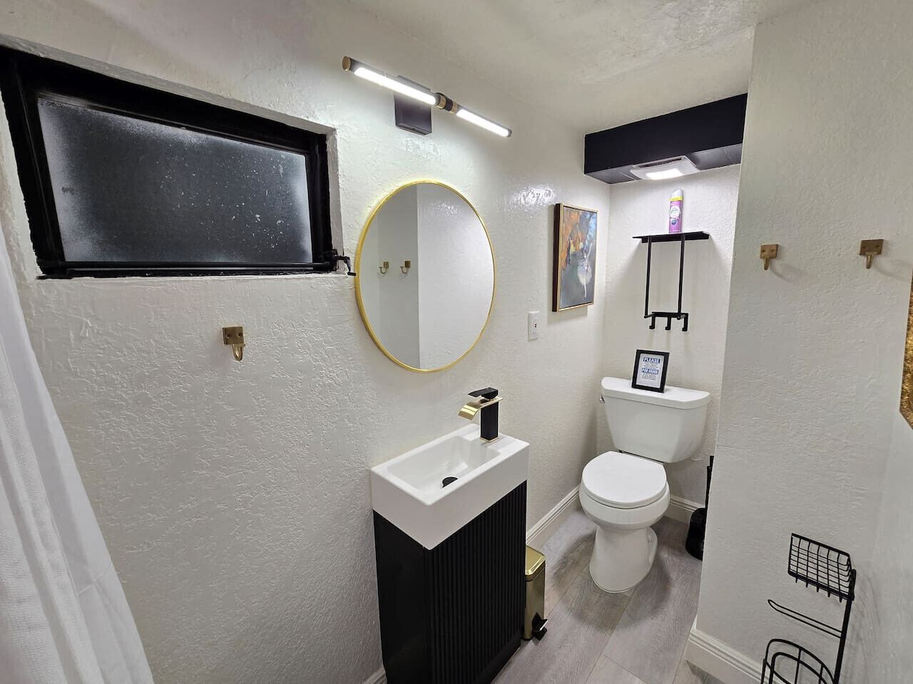 Une petite salle de bain avec un lavabo blanc, un miroir rond, des toilettes et une petite étagère contenant des articles de toilette.