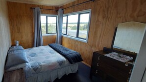 Une chambre à coucher avec un lit, une commode et deux fenêtres.