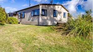 Une maison de plain-pied avec un toit en pente, une antenne parabolique et un petit jardin devant, avec de la pelouse et un arbuste.