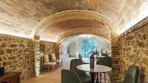 Una stanza con pareti in pietra, un tavolo rotondo con sedie, una cantina e vista attraverso un'ampia finestra ad arco.