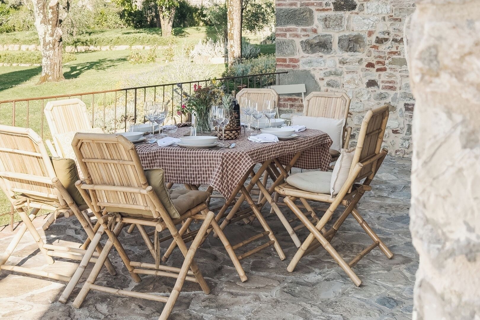 An outdoor dining area with a stone floor, wooden chairs, and a checkered tablecloth.