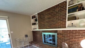 Ein modernes Wohnzimmer mit Kamin aus Ziegelsteinen, klaren Kunststoffstühlen und einem Bücherregal.