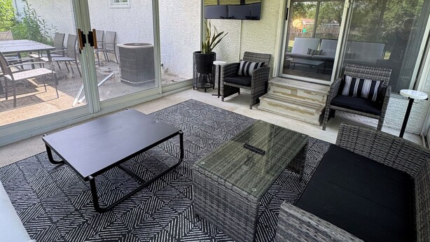 Ein überdachter Patio-Bereich mit Gartenmöbeln, einem an der Wand befestigten Flachbildfernseher und einer Glastür zum Garten.