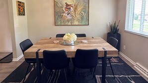 Ein Essbereich mit Holztisch, schwarzen Stühlen, einer Pendelleuchte, einem Tigergemälde und einem Fenster mit Jalousien.
