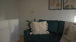 Una sala de estar con un sofá color turquesa, una manta blanca y una planta verde.