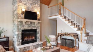 A living room with a stone fireplace, a wooden staircase, and a cozy seating area. - Hot Tub, Deck w/ Breathtaking Mountain Views (Swannanoa)