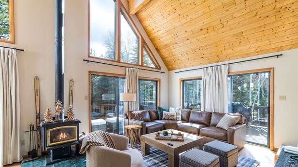 Ein geräumiges Wohnzimmer mit Kamin, Ledersofas und großen Fenstern mit Blick auf den Wald.