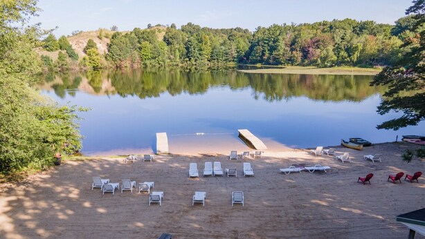A lakeside beach with lounge chairs, a picnic table, and boats. - Goshorn Lake #1! Beach Access - Shared Pool - 1 min from Dune Rides (Saugatuck)