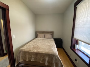 A small, narrow room with a single bed, a nightstand, and a window with blinds. - Sweet 2-bedroom + den apartment with AC in vibrant Bucktown (Chicago)