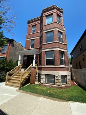 A multi-story brick building with a central entrance and a staircase leading to the ground floor. - Sweet 2-bedroom + den apartment with AC in vibrant Bucktown (Chicago)