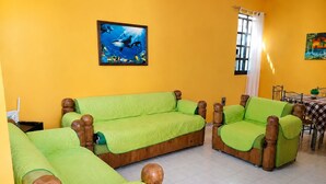 Ein Zimmer mit einer gelben Wand, zwei grünen Sofas, einem Holztisch mit kariertem Tischläufer und einem Bild von Fischen.